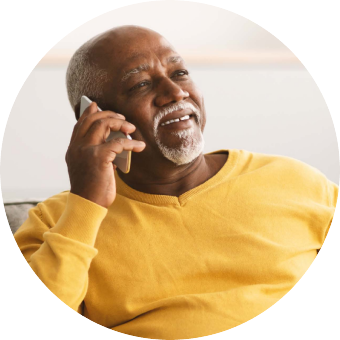 An older man in a yellow sweater smiling while talking on the phone