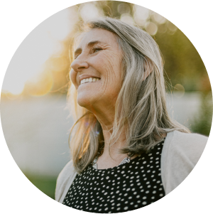 A middle-aged woman with gray-blonde hair smiling and looking upward outdoors in warm sunlight